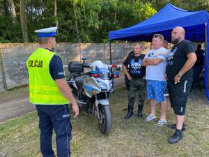 Na zdjęciu znajduje się policjant podczas rozmowy z uczestnikami zlotu motocyklowego