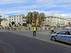 policjant zabezpiecza przejazd rowerzystów, stoi na jezdni, blokuje przejazd samochodom