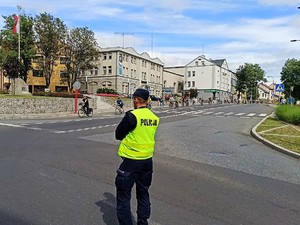 policjant zabezpiecza przejazd rowerzystów, stoi na jezdni, blokuje przejazd samochodom