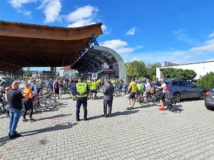 na terenie skweru stoi grupa rowerzystów, przed nimi stoi umundurowany policjant, przygląda się im