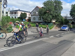 policjant zabezpiecza przejazd rowerzystów, stoi na jezdni, blokuje przejazd samochodom