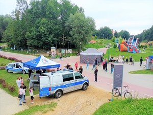 zdjęcie wykonane z oddali, widać policyjne stanowisko z policyjnym namiotem, radiowozem, a w tle widać inne namioty, kolorowy dmuchaniec dla dzieci i uczestników festynu charytatywnego