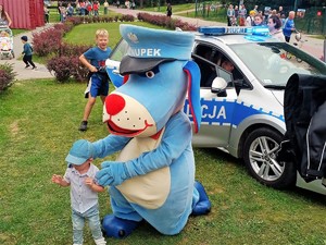 maskotka śląskiej policji, pies Sznupek pozuje do zdjęcia z chłopcem, w tle widać policyjny radiowóz