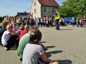 policjant prowadzi spotkanie profilaktyczne z dziećmi, dzieci stoją przed nim na boisku szkolnym