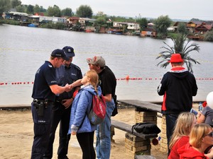 dwaj policjanci rozmawiają z kobietą i mężczyzną, uczestnikami festynu, stoją na plaży piaszczystej przy zbiorniku wodnym