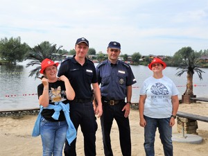 policjanci pozują do wspólnego zdjęcia z uczestniczkami festynu, stoją na piaszczystej plaży blisko zbiornika wodnego