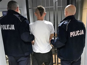 dwaj policjanci trzymają zatrzymanego mężczyznę, wszyscy stoją tyłem