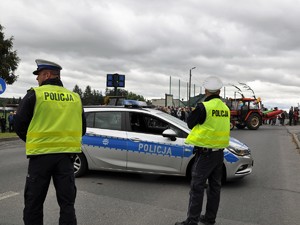 obok radiowozu stoją policjanci, zabezpieczają przejazd dożynkowego korowodu