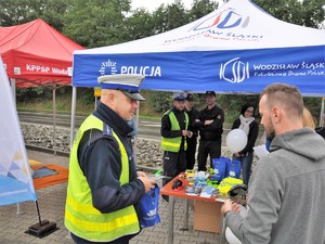 policjant rozmawia z mężczyzną, w tle pod specjalnym namiotem stoją przedstawiciele służb, policjanci i strażacy