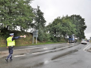 policjant stoi na drodze, tarczą do zatrzymywania pojazdów, daje sygnał kierowcy pojazdu ciężarowego do zatrzymania