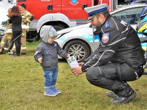 policjant kuca przed chłopczykiem, który wkłada pieniądz do puszki charytatywnej