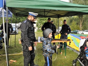 policjant stoi za chłopcem, który trzyma w rękach broń długą