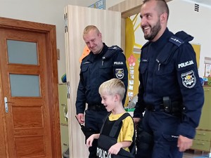 obok policjantów stoi przedszkolak, ma na sobie założoną kamizelkę z napisem &quot;Policja&quot;