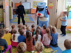 przed grupą dzieci siedzących na podłodze stoi policjant i szunupek, maskotka śląskiej policji