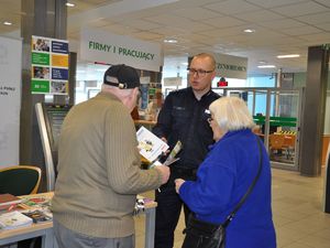 policjant stoi przed parą seniorów, przekazuje im materiały profilaktyczne