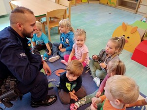 policjant kuca przed przedszkolakami, dziewczynka ma na rękach założone kajdanki, uśmiecha się