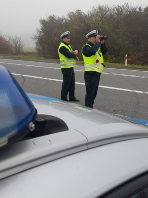 dwaj funkcjonariusze inspekcji ruchu drogowego obserwują ruch drogowy, stoją na poboczu obok radiowozu