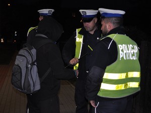 trzej policjanci stoją przed młodym mężczyznom, jeden z nich przekazuje mu opaskę odblaskową