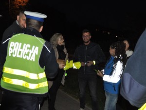policjant i kobiety stoją przed dwoma napotkanymi mężczyznami, przekazują im odblaskowe opaski
