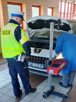 policjant stoi obok pojazdu, przygląda się włączonym reflektorom samochodowym