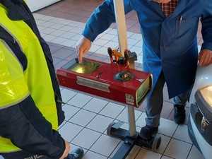 mężczyzna przykłada urządzenie do sprawdzanie stanu oświetlenia samochodu, obok niego stoi policjant