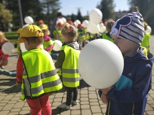 na zdjęciu widać małe dzieci, które trzymają w rękach balony, większość ma na sobie ubrane kamizelki odblaskowe