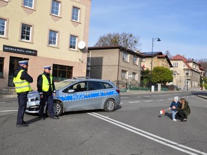 na skrzyżowaniu stoi radiowóz i dwaj policjanci, obok radiowozu stoi chłopczyk z mamą