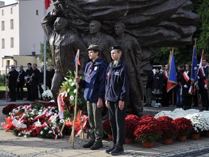 przed pomnikiem Powstańców Śląskich leżą wiązanki kwiatów, obok stoją harcerze