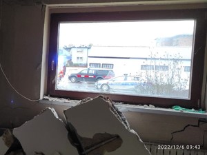Okno pomieszczenia przez które widać policyjny radiowóz oraz wóz straży pożarnej.