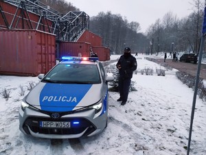 obok policyjnego radiowozu stoi policjant