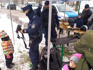 podczas festynu policjanci rozmawiają z uczestnikami, policjant prezentuje małemu dziecku jednostkę broni długiej