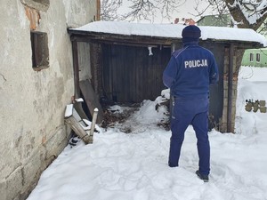 policjant podchodzi do prowizorycznej dobudówki, na ziemi leży śnieg