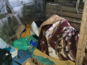 Zdjęcie przedstawia mężczyznę w pomieszczeniu gospodarczym leżący na  prowizorycznym legowisku.