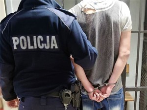 policjant stoi obok zatrzymanego mężczyzny, stoją obok siebie tyłem do zdjęcia