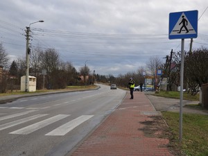 policjant kontroluje prędkość pojazdów, stoi na poboczu i trzyma urządzenie do pomiaru prędkości