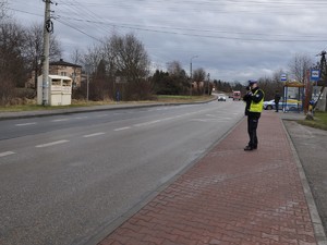 policjant stoi na chodniku i kontroluje urządzeniem prędkość, z jaką poruszają się pojazdy