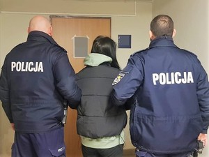 dwaj policjanci trzymają za ramię stojącą tyłem zatrzymaną kobietę