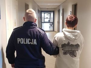 na korytarzu policjant trzyma za ramię zatrzymaną kobietę