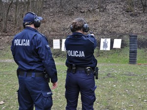 policjant stoi obok policjantki, która wykonuje trening strzelecki