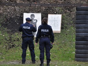 policjant i policjantka stoją przed tarczą, oglądają przestrzeliny