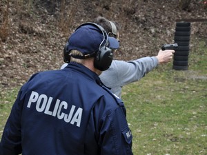 policjant przygląda się strzelającemu nieumundurowanemu policjantowi, mężczyźni stoją tyłem do zdjęcia