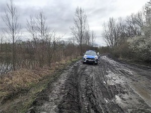 na szutrowej drodze stoi radiowóz, widać zarośla i zbiornik wodny