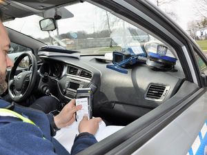 policjant siedzi w radiowozie, w ręku trzyma terminal płatniczy i wydruk