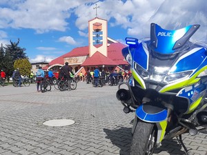 na pierwszym planie stoi policyjny motocykl, w tle zbierają się uczestnicy rajdu rowerowego