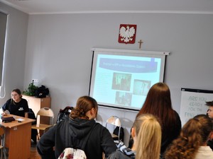 uczestnicy słuchają wykładu prezentowanego przez uczennicę klasy mundurowej, która wyświetla slajdy prezentacji multimedialnej