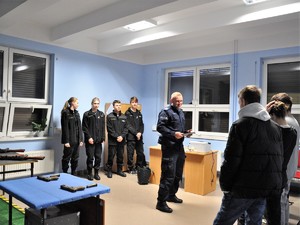 w sali strzelnica multimedialna policyjny instruktor stoi przez gości &quot;Dni otwartych&quot;, w rękach trzyma klawiaturę, za nim stoją uczniowie klasy mundurowej