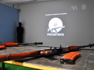 na stole leżą dwie jednostki broni, w tle wyświetla się program do treningu strzeleckiego