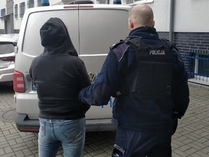 policjant trzyma zatrzymaną kobietę, stoją tyłem przy policyjnym radiowozie