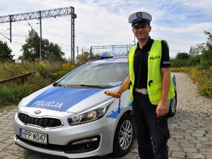 policjant stoi obok radiowozu, w ręku trzyma alkomat, uśmiecha się