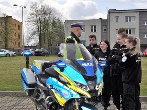 obok policyjnego motocykla stoi policjant i uczniowie klas mundurowych